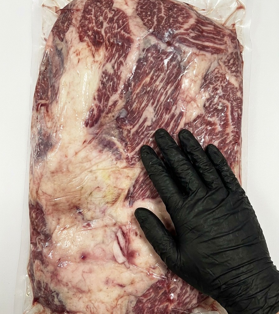 Vista de cerca de un cuchillo retirando el exceso de grasa gruesa de la superficie de un brisket de Wagyu Stone Axe crudo.