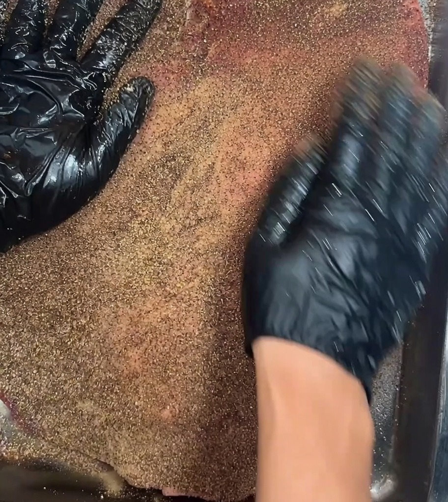 El brisket sazonado reposando sobre una rejilla dentro de un refrigerador para el marinado nocturno.