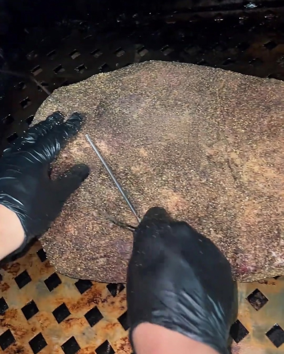 Vista de cerca de una sonda de termómetro insertada en la sección más gruesa del brisket crudo y sazonado.