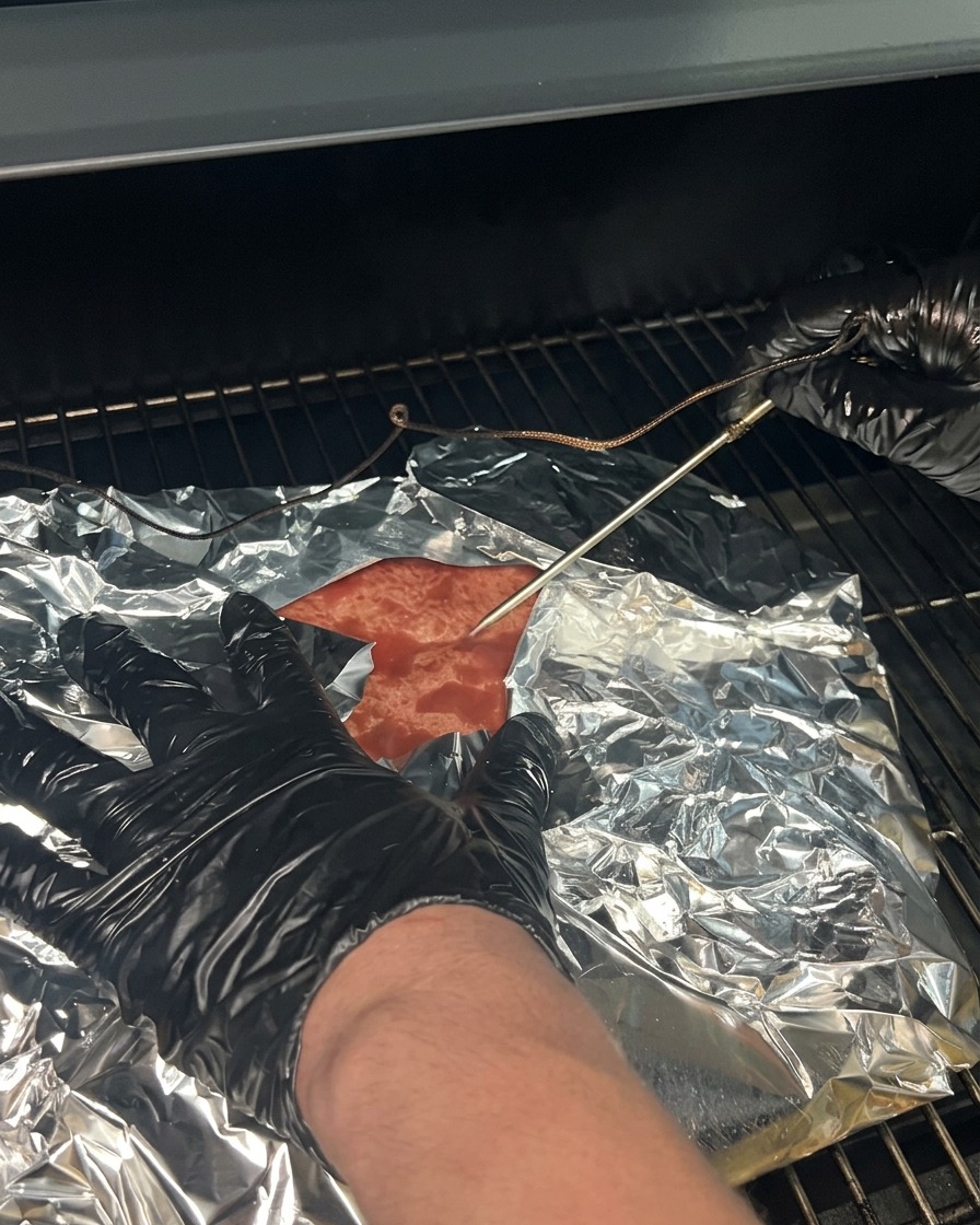 El brisket envuelto colocado de nuevo en las rejillas del ahumador con la sonda del termómetro reinsertada.