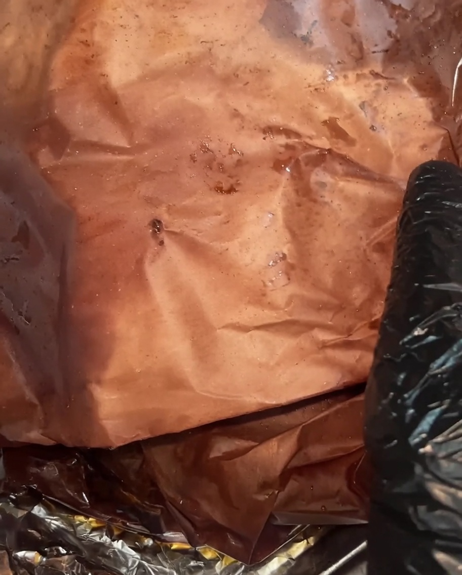 El brisket completamente cocido desenvuelto, mostrando una corteza oscura y húmeda y jugos ricos acumulados en el papel de carnicero.