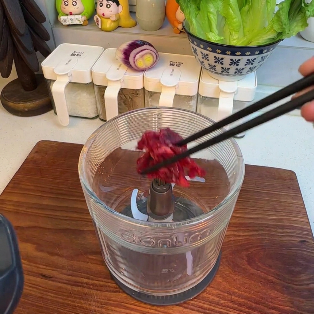 Carne de ternera picada dentro del recipiente de un procesador de alimentos.