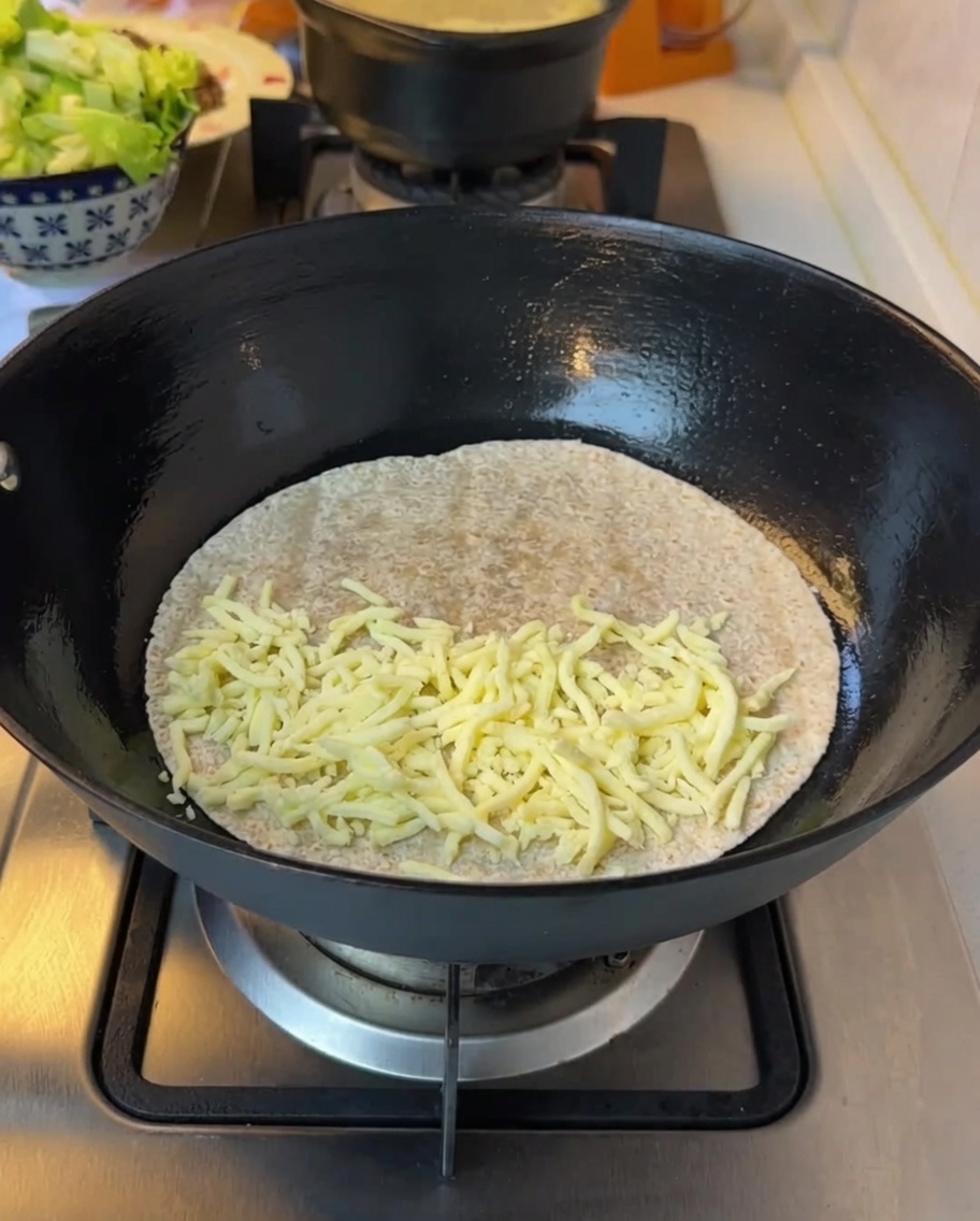 Lechuga picada siendo añadida sobre el queso derretido en la tortilla.