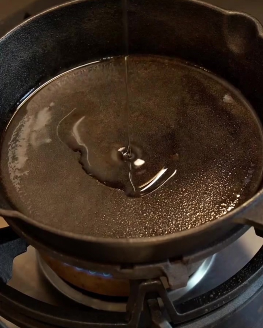 Cebolla y ajo picados sofriéndose hasta quedar traslúcidos en una sartén de hierro fundido con aceite.