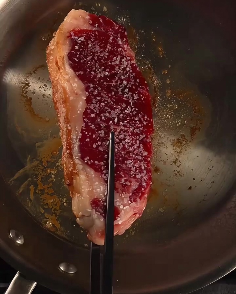 Filete en una sartén siendo bañado con mantequilla, ajo y ramitas de romero fresco.