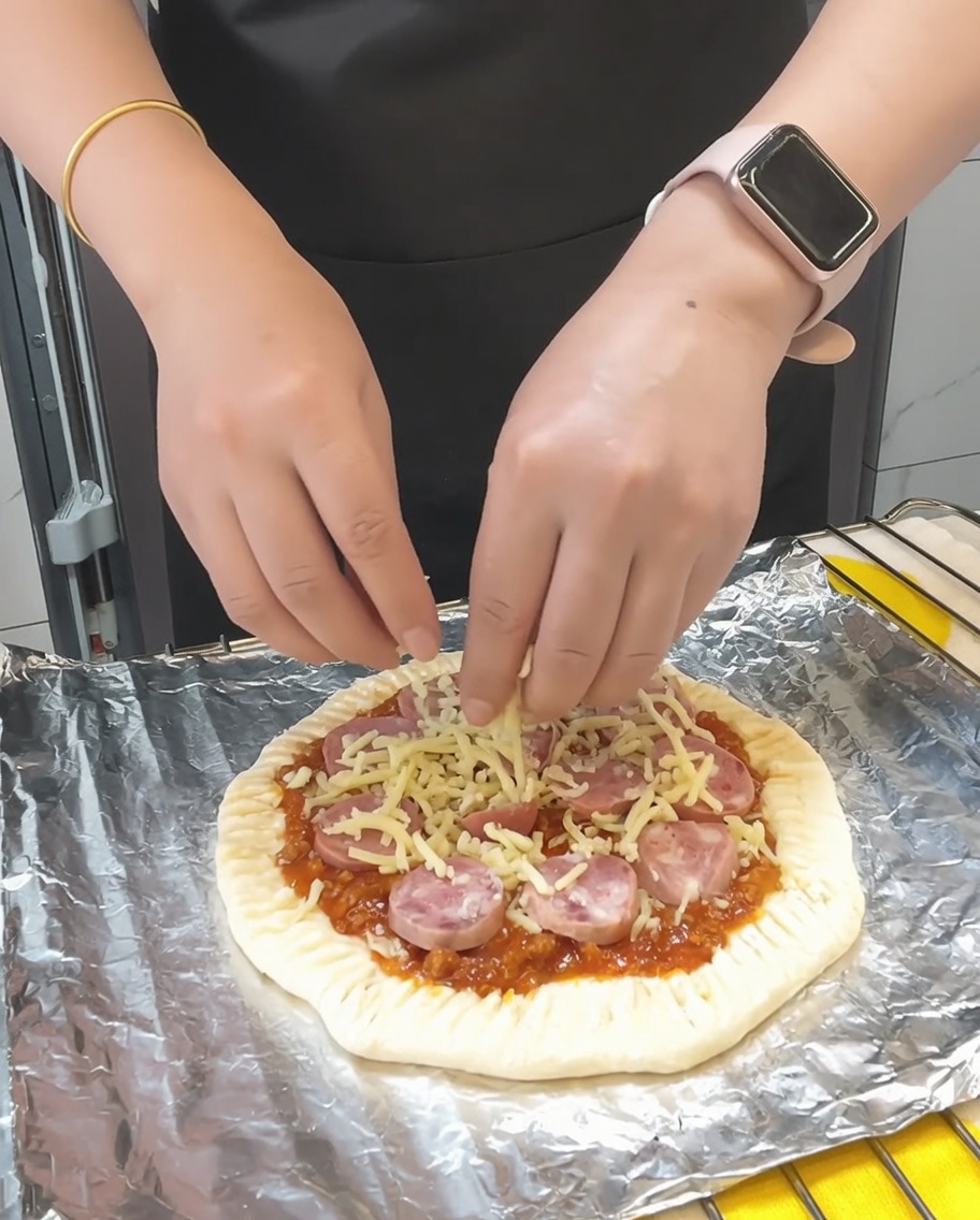 Último puñado de queso mozzarella esparcido sobre la pizza, seguido de un toque de perejil seco.
