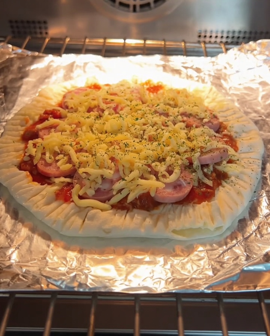 Una pizza de panqueque de cebollín recién horneada con queso fundido y rodajas de salchicha, dentro del horno en una rejilla.