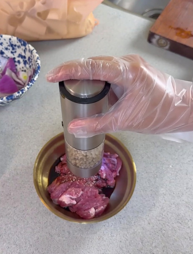Moliendo pimienta fresca sobre cerdo cortado en un pequeño bol metálico con salsa de soja.