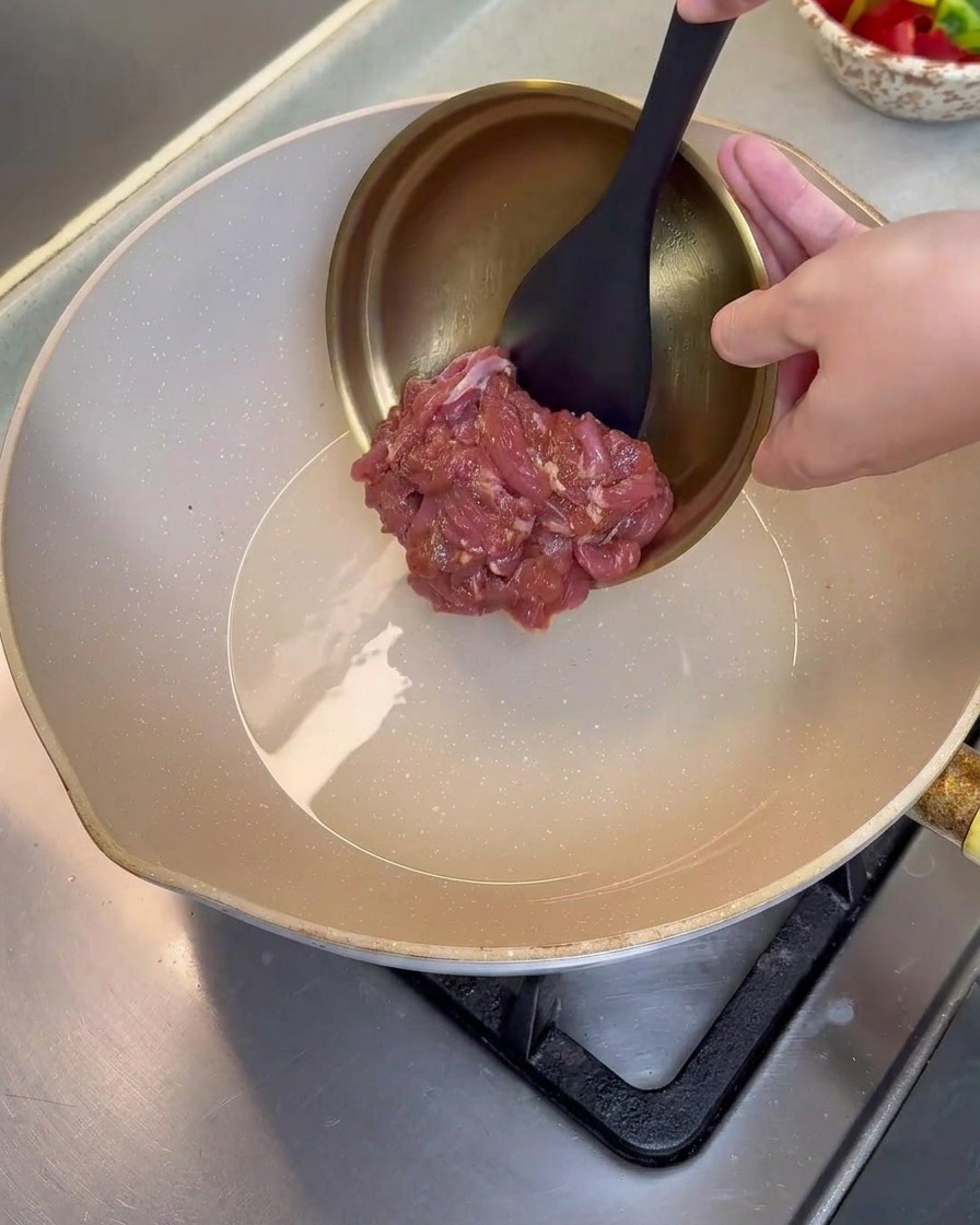 Tiras de cerdo marinado siendo vertidas en una sartén caliente con aceite.