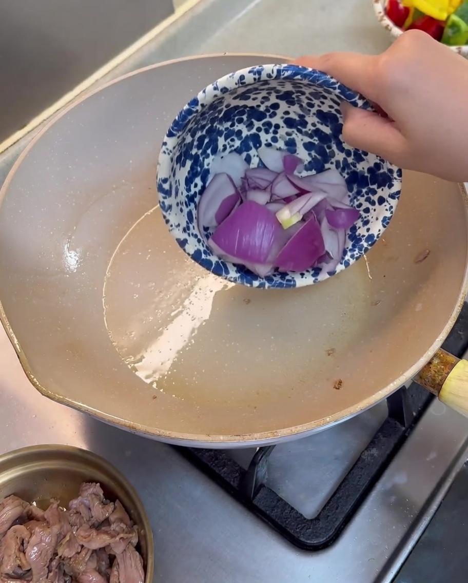 Trozos de cebolla morada siendo salteados en una sartén aceitada.