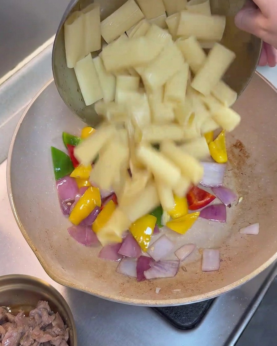 Pasta rigatoni cocida siendo añadida a la sartén con pimientos y cebollas.
