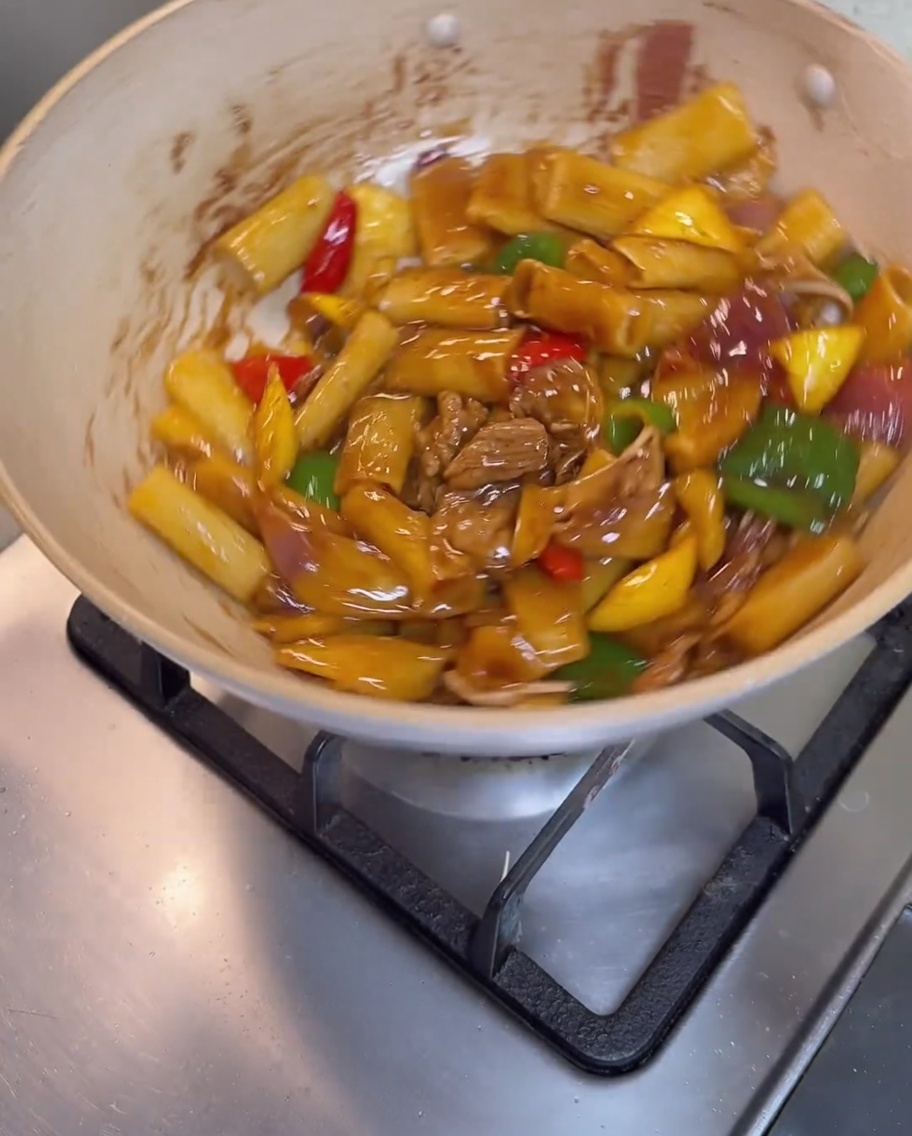 Pasta, carne y verduras siendo mezcladas en la sartén hasta cubrirse con una salsa brillante.