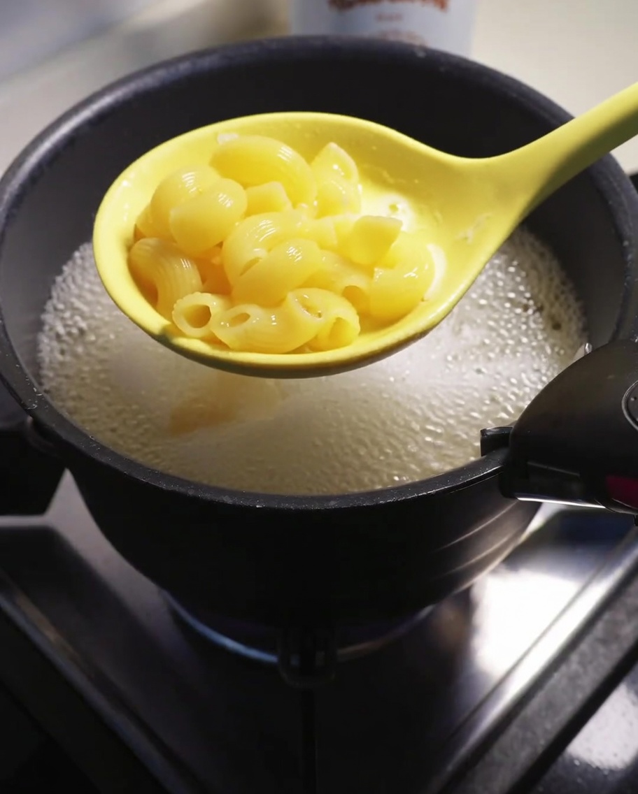 Macarrones cocidos siendo retirados del agua hirviendo con una espumadera.