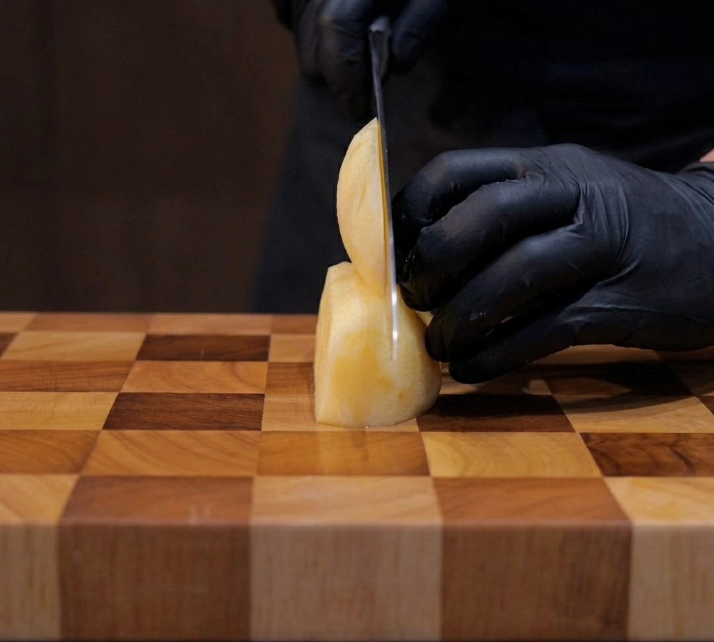 Papas siendo cortadas cuidadosamente en cubos de un centímetro sobre una tabla de madera.