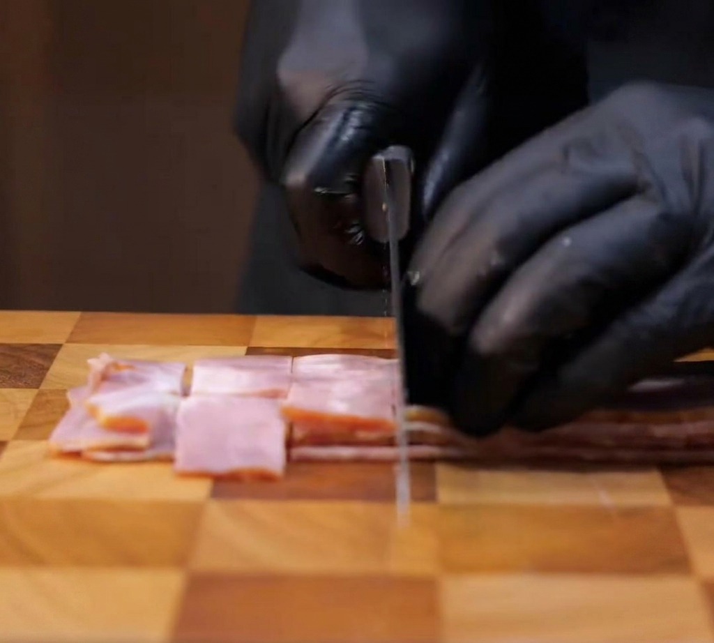 Tiras de tocino siendo cortadas en trozos cuadrados sobre una tabla de madera.