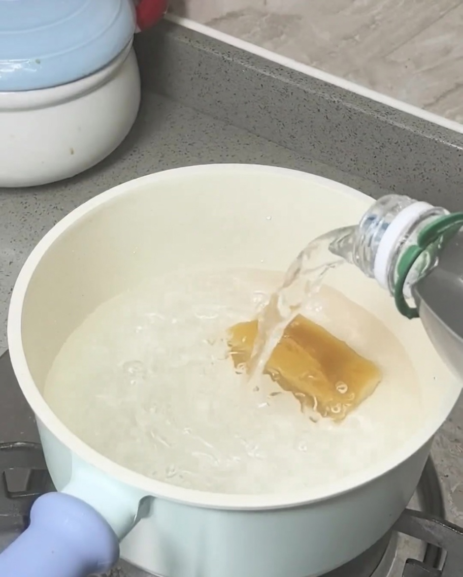 Bloque de azúcar moreno derritiéndose en agua hirviendo dentro de una olla de color claro.
