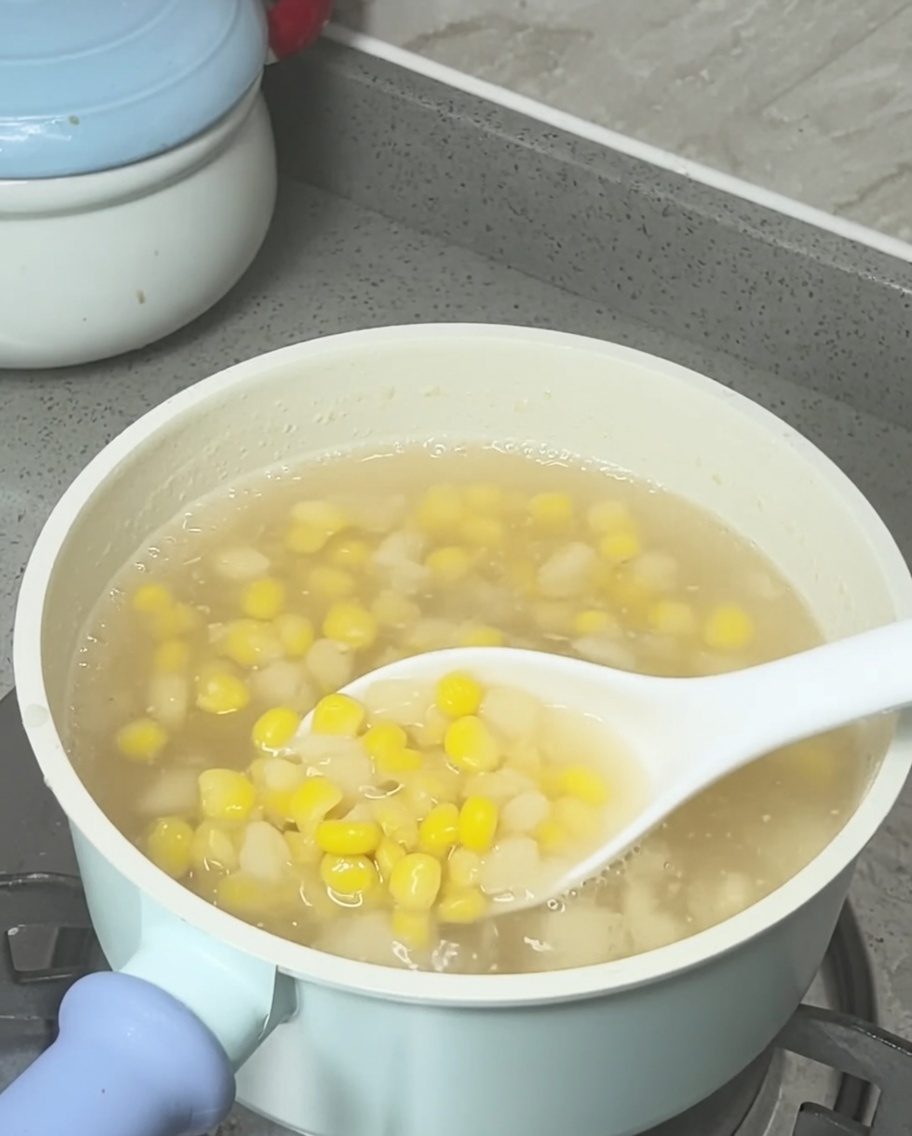 Leche de coco siendo vertida sobre la olla de sopa de maíz y castañas de agua terminada.