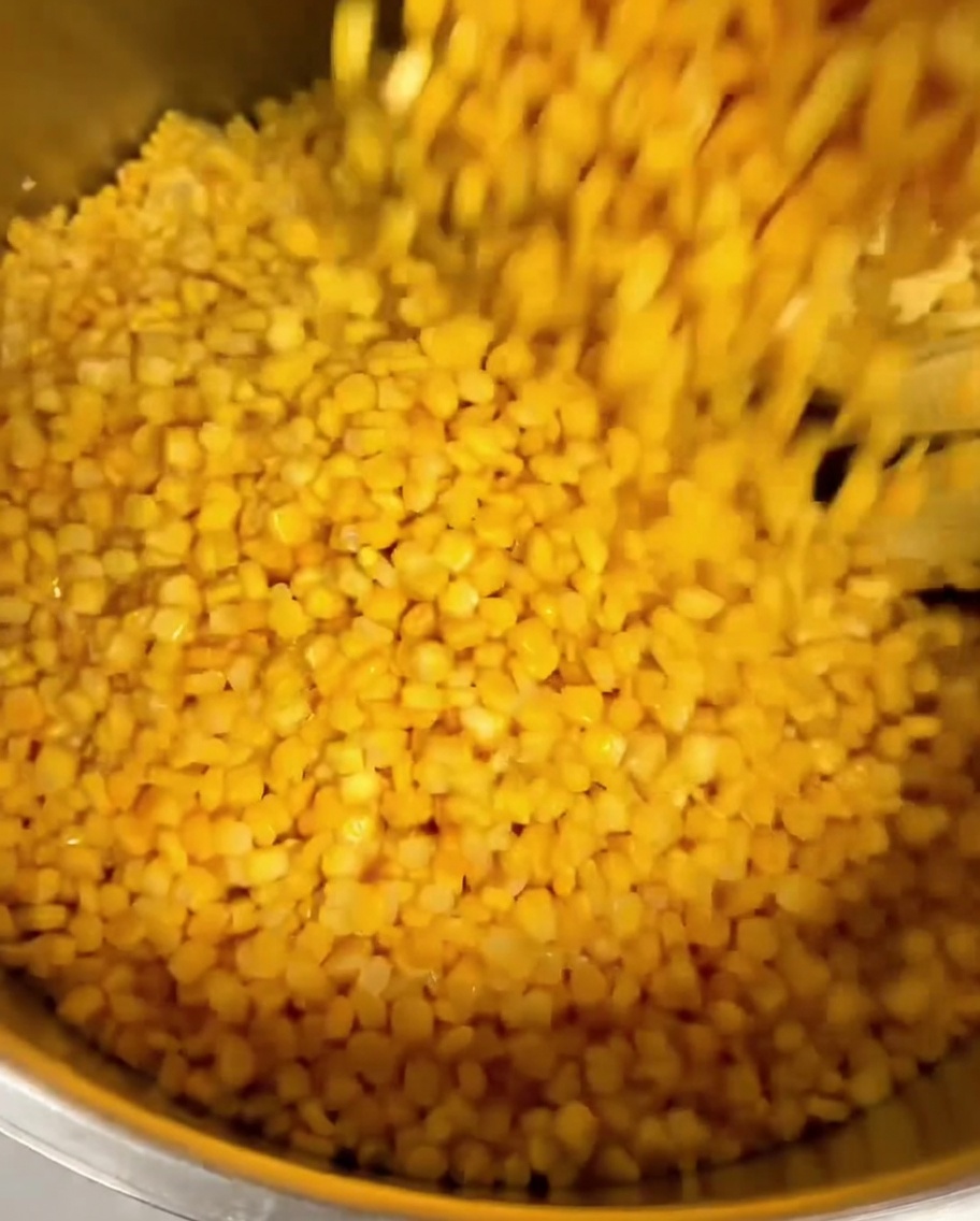 Maíz enlatado siendo vertido sobre granos de elote fresco en una olla grande de metal.