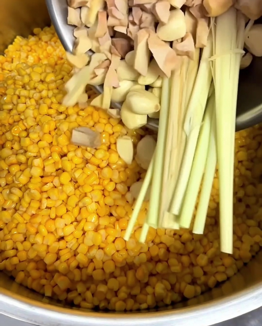 Galangal picado, dientes de ajo enteros y hierba limón añadidos a una olla con granos de elote.