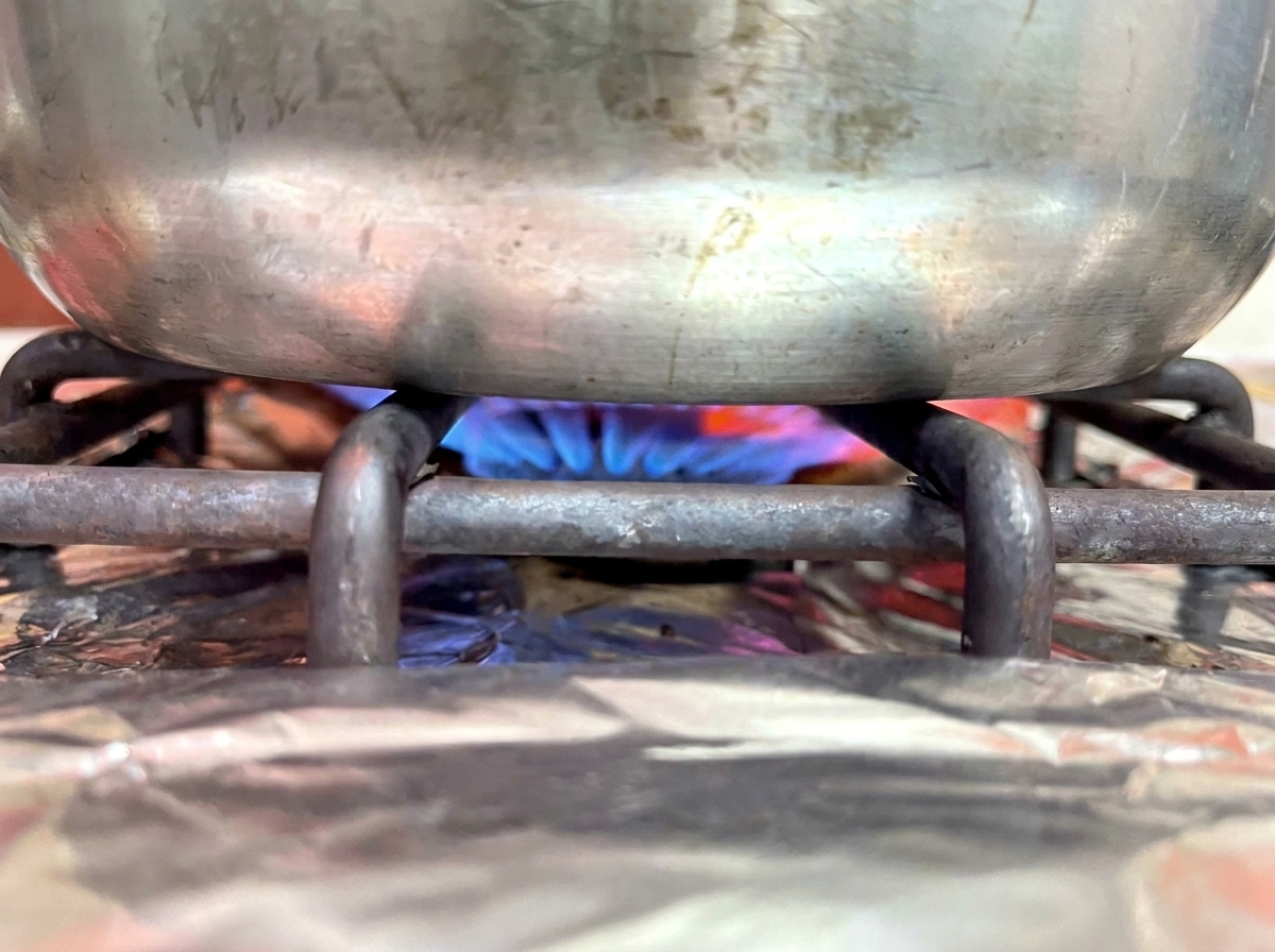 Base de una olla sobre la hornilla de una estufa de gas con una flama azul.
