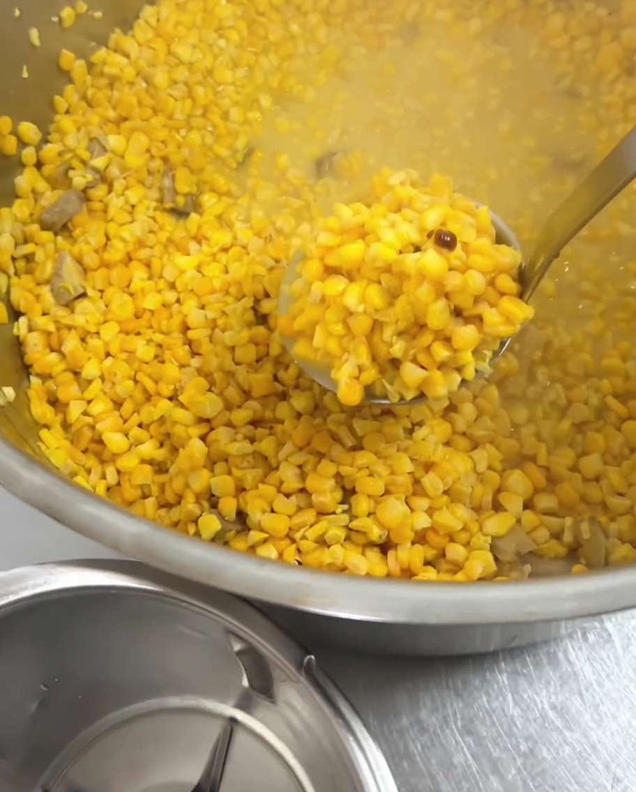 Un cucharón de metal recogiendo granos de elote cocidos de la olla.