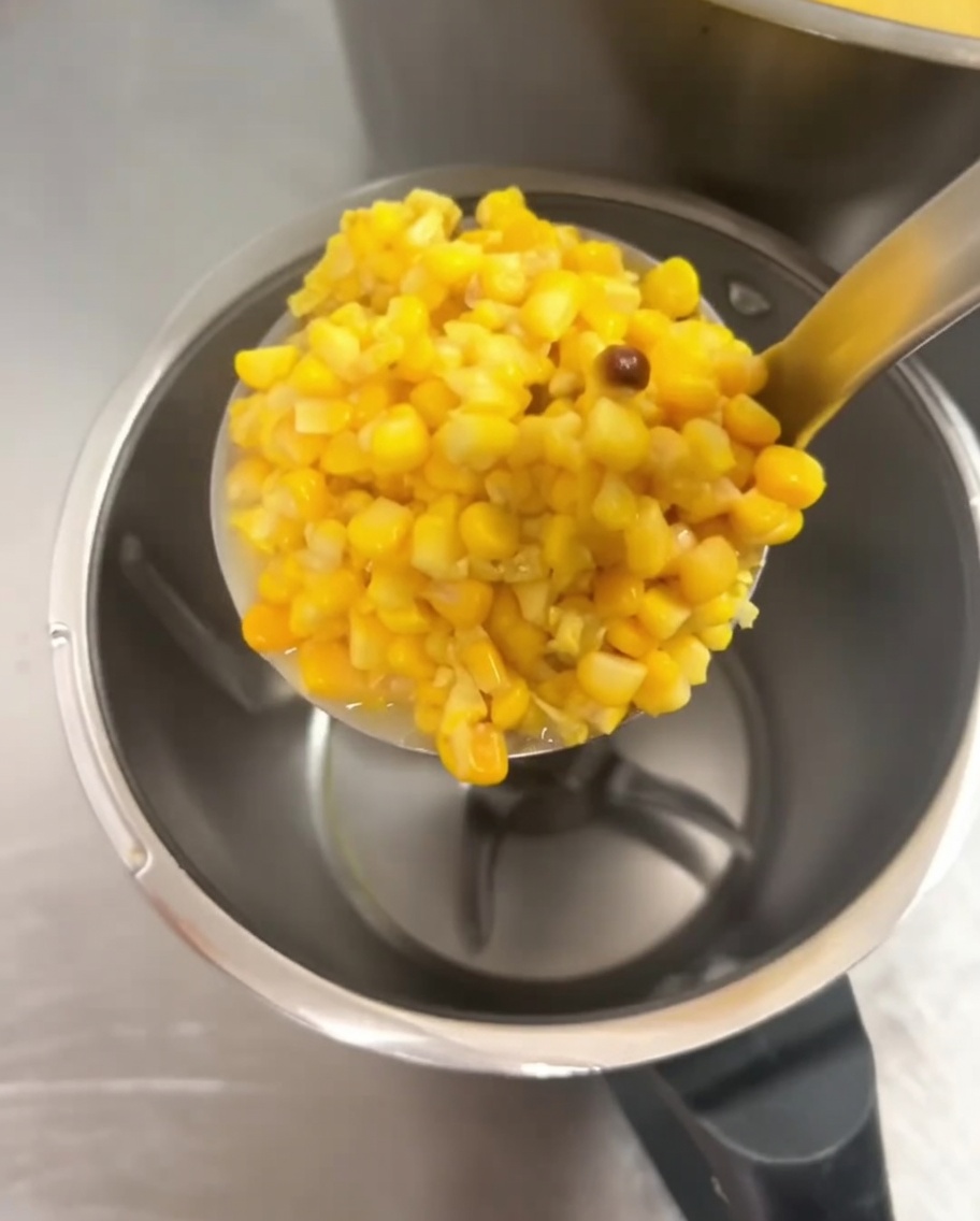 Granos de elote cocidos siendo añadidos al vaso de una licuadora.
