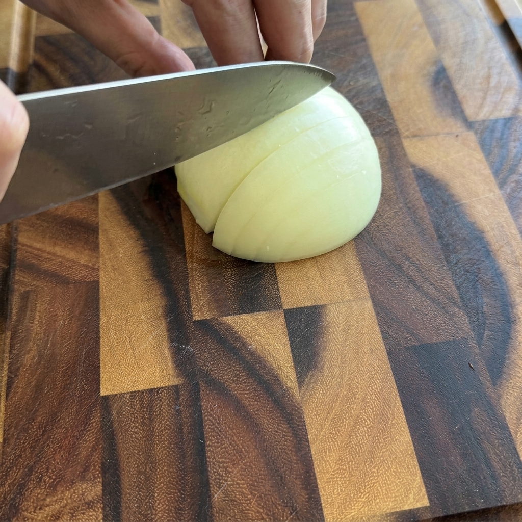 Una persona cortando la mitad de una cebolla blanca en trozos pequeños sobre una tabla de cortar de madera.