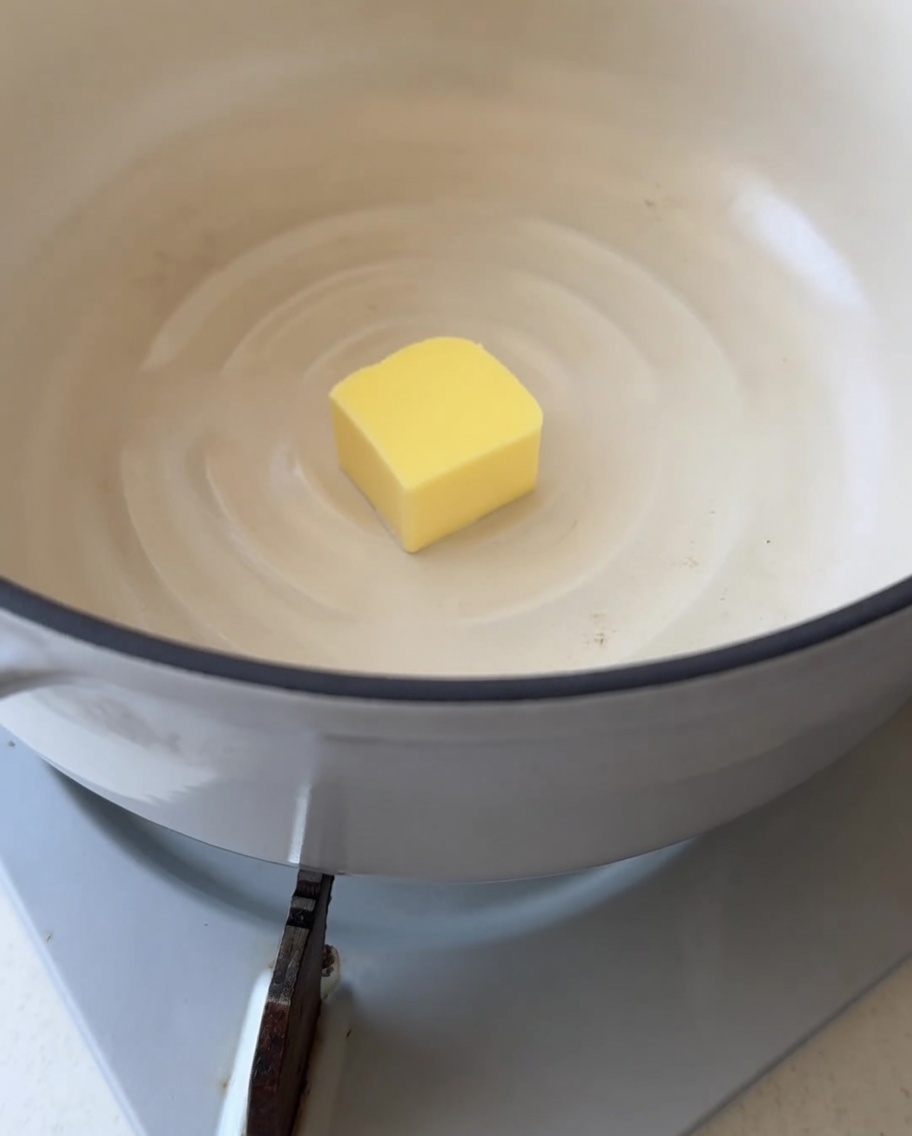 Primer plano de un cuadro de mantequilla amarilla comenzando a derretirse en una olla blanca y limpia.