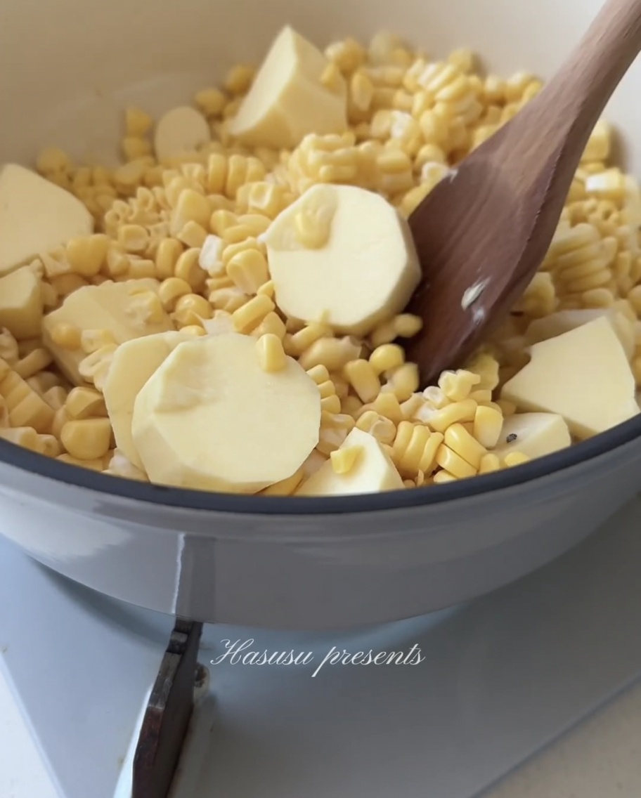 Una cuchara de madera revolviendo una mezcla de granos de maíz amarillo y trozos de batata blanca en una olla.