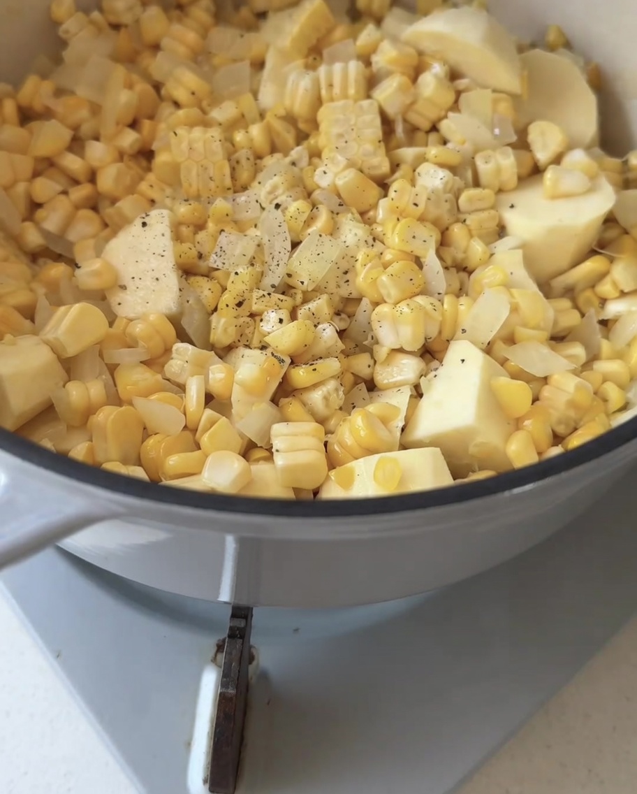 Pimienta negra recién molida cayendo sobre una mezcla de maíz, cebolla y batata en una olla de cocción.