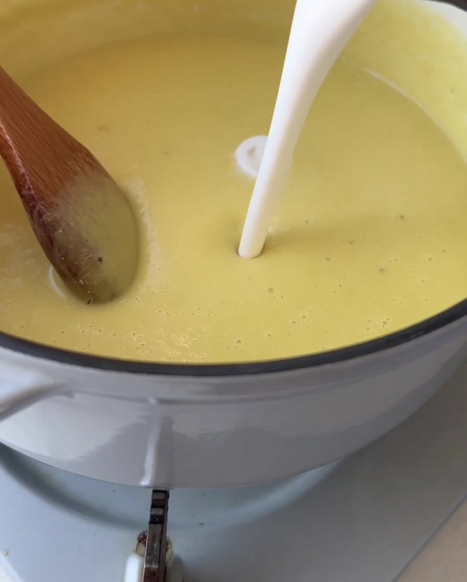 Crema blanca siendo vertida en una olla de sopa de maíz suave y de un amarillo brillante.