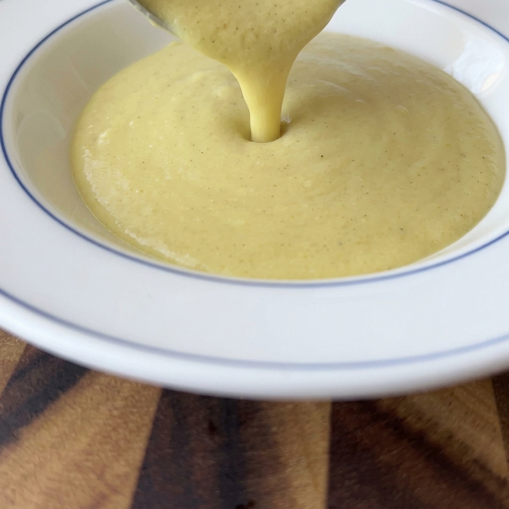 Sopa espesa y cremosa de maíz amarillo siendo vertida desde un cucharón en un tazón blanco con borde azul.