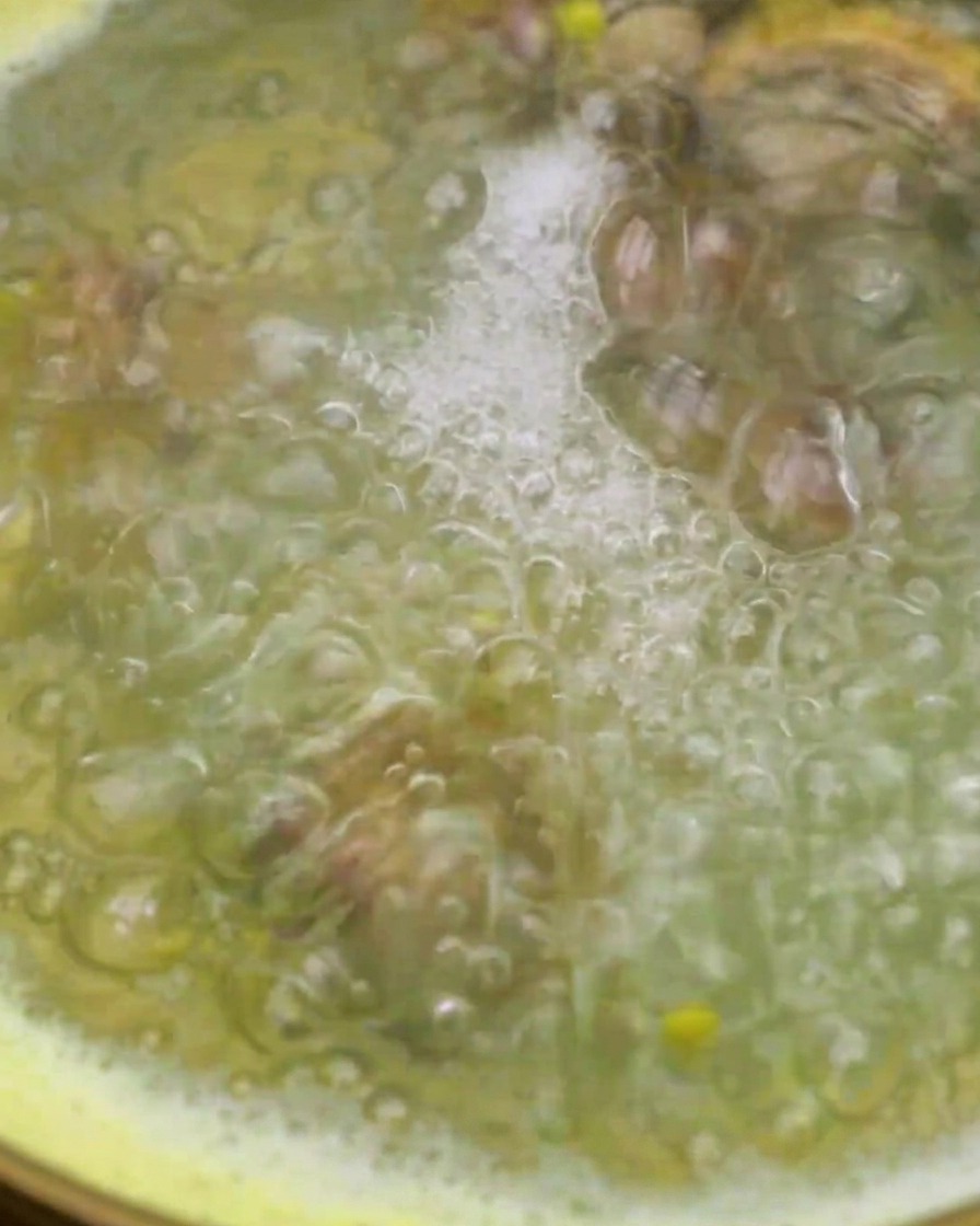 Almejas siendo añadidas a una olla con el agua de maíz hirviendo usando un colador de malla.