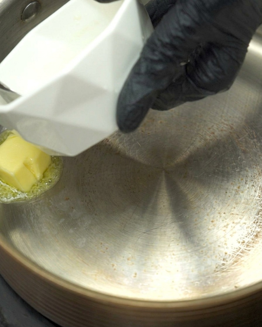 Mantequilla derretida en un cazo con ajo picado y harina siendo salteados.