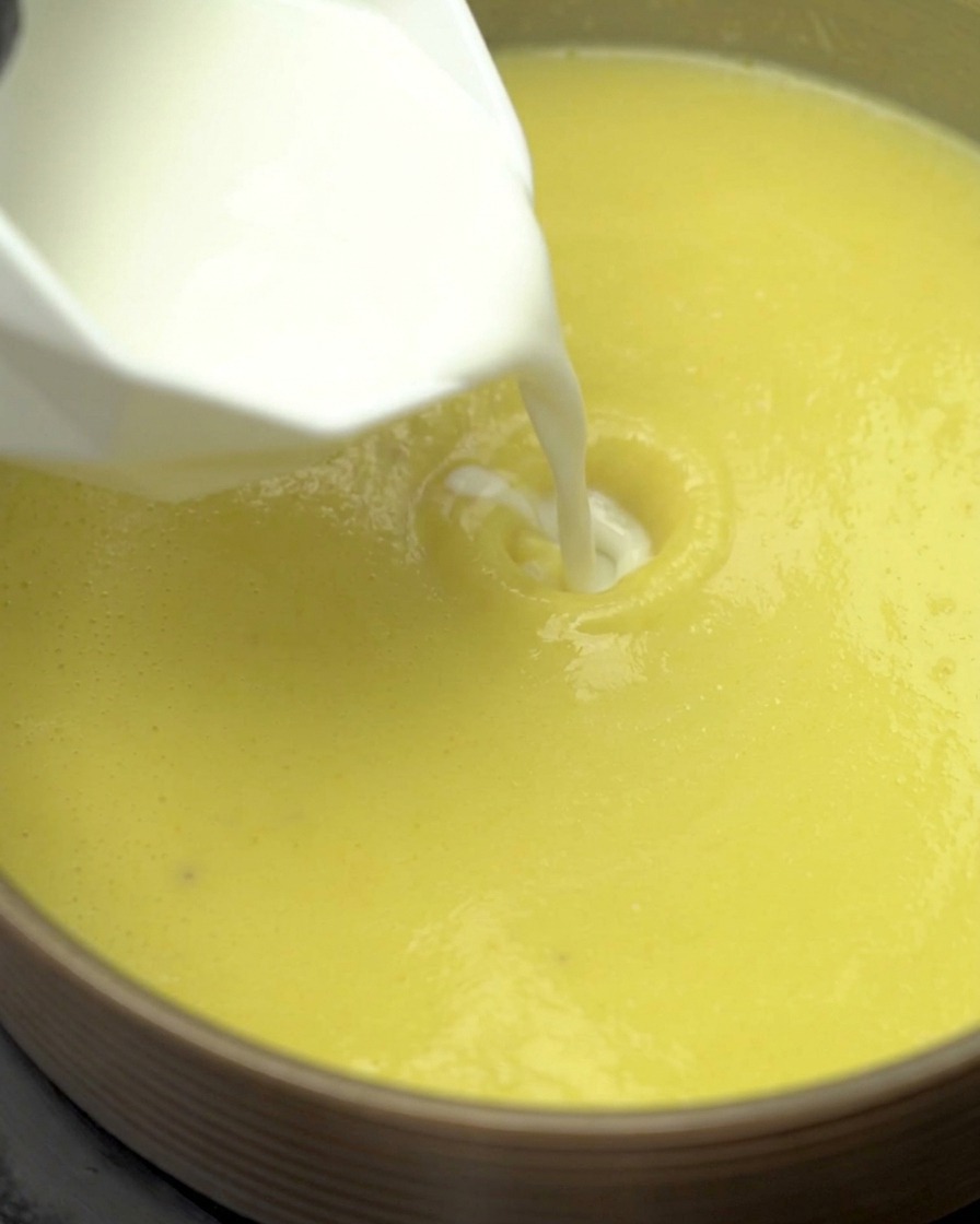 Leche y crema ligera siendo vertidas en la base de sopa de maíz hirviendo a fuego lento en una olla.