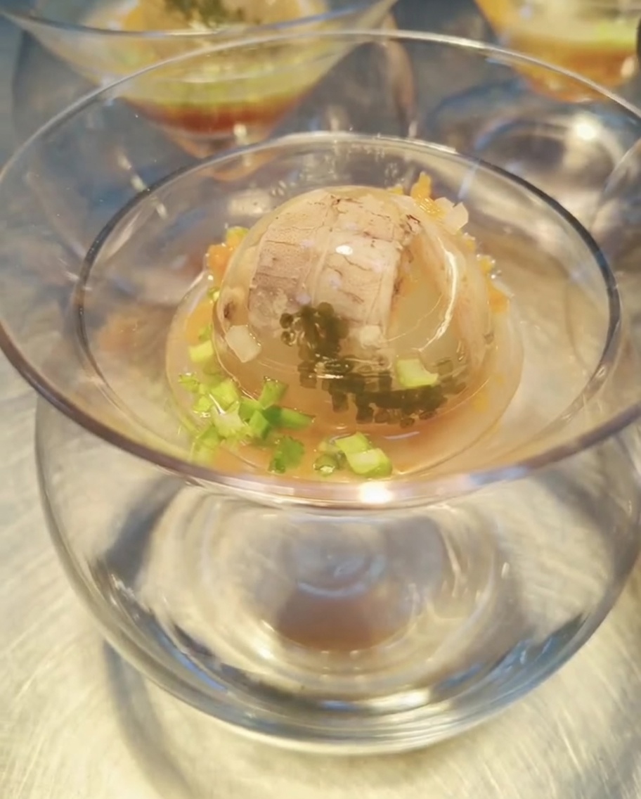 Una esfera de gelatina de marisco en un cuenco, siendo rociada con una salsa ámbar y lista para decorar.