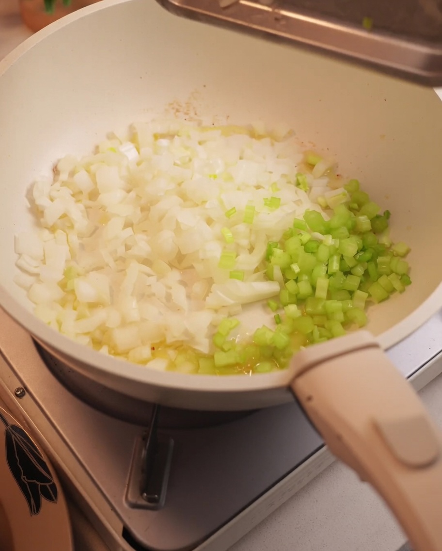 Cebolla y apio picados sofriéndose en un sartén.