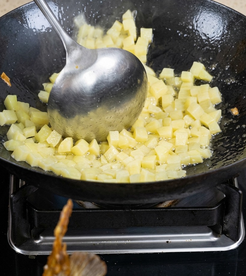 Patatas en cubos salteándose en un wok con aceite hasta dorarse ligeramente.