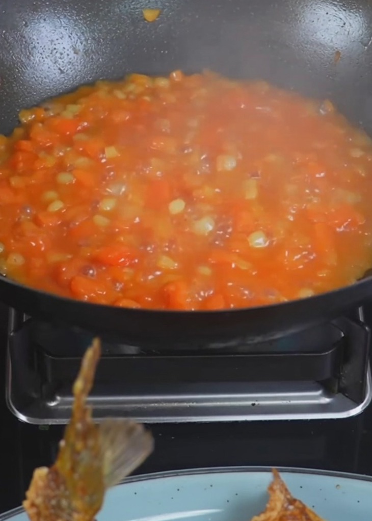 Agua hirviendo siendo vertida en un wok que contiene patatas y tomates cocinados.