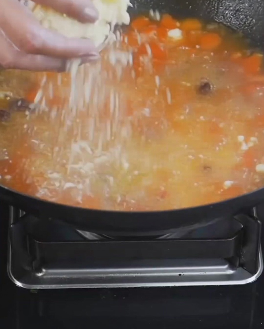 Bolitas de harina y huevo siendo espolvoreadas en una olla de sopa hirviendo a fuego lento con tomates y patatas.