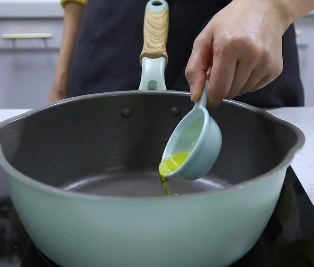 Vertiendo aceite de nuez desde una pequeña cuchara medidora en una olla.