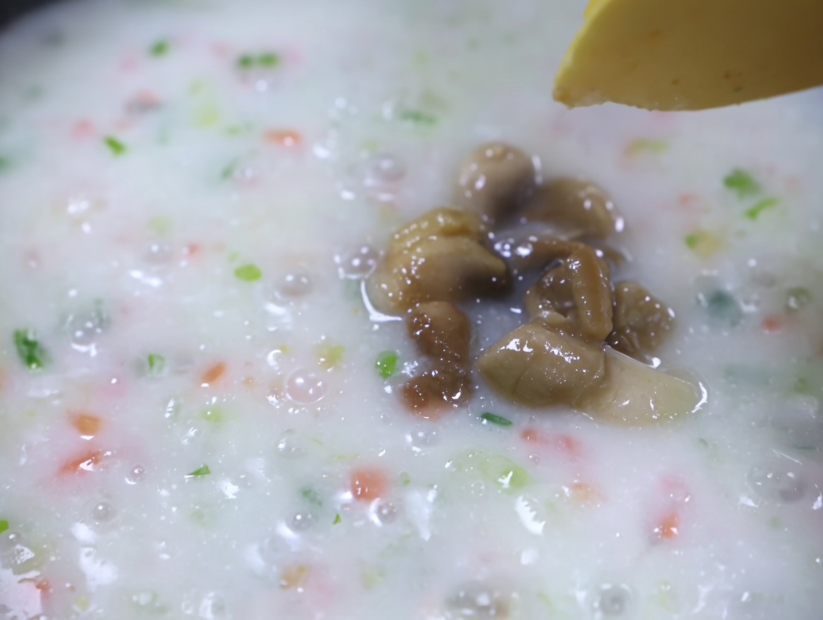 Carne de almeja cocida añadiéndose a una sopa de verduras cremosa a fuego lento.