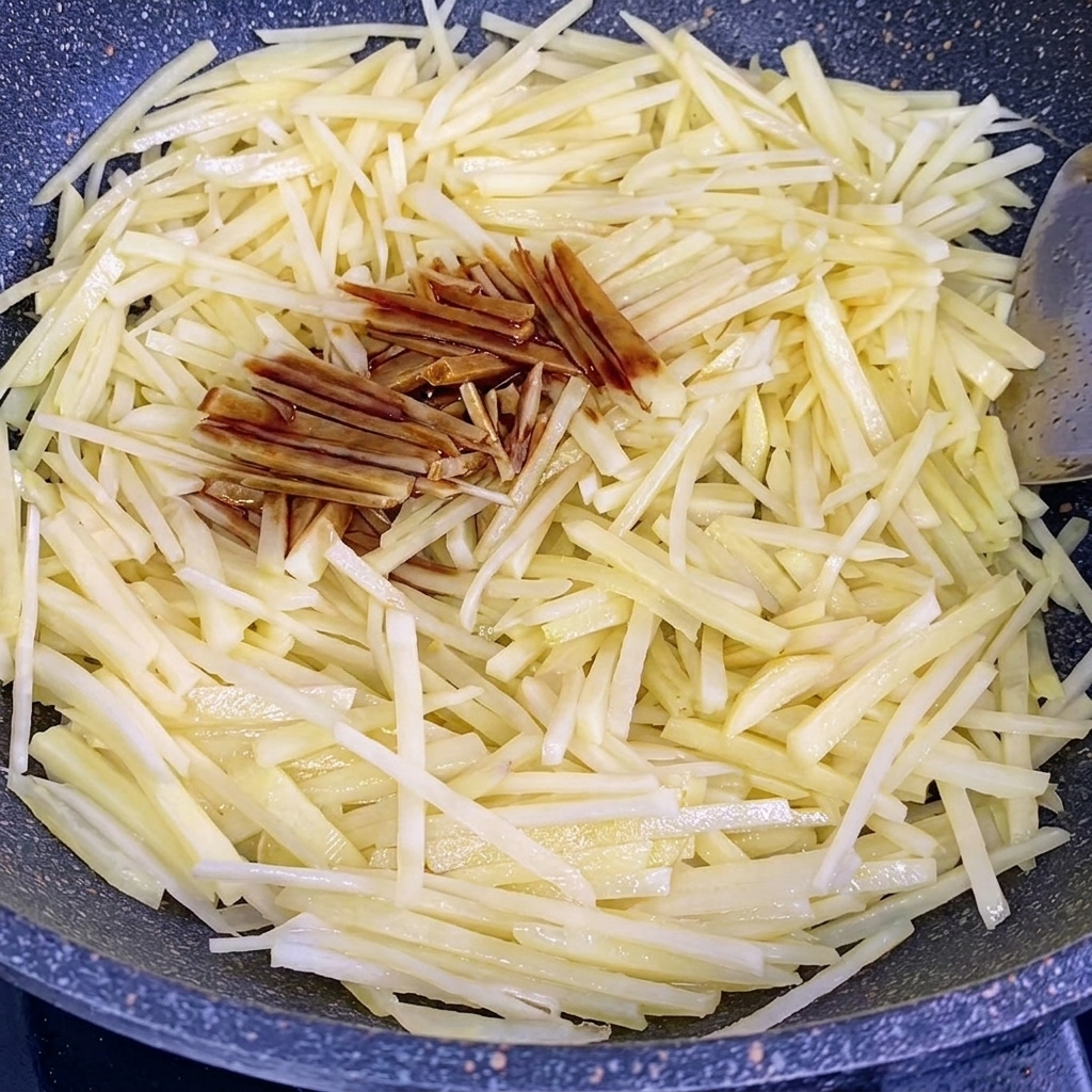Salsa de soja y salsa de ostras vertiéndose sobre las tiras de papa que se saltean en un wok.