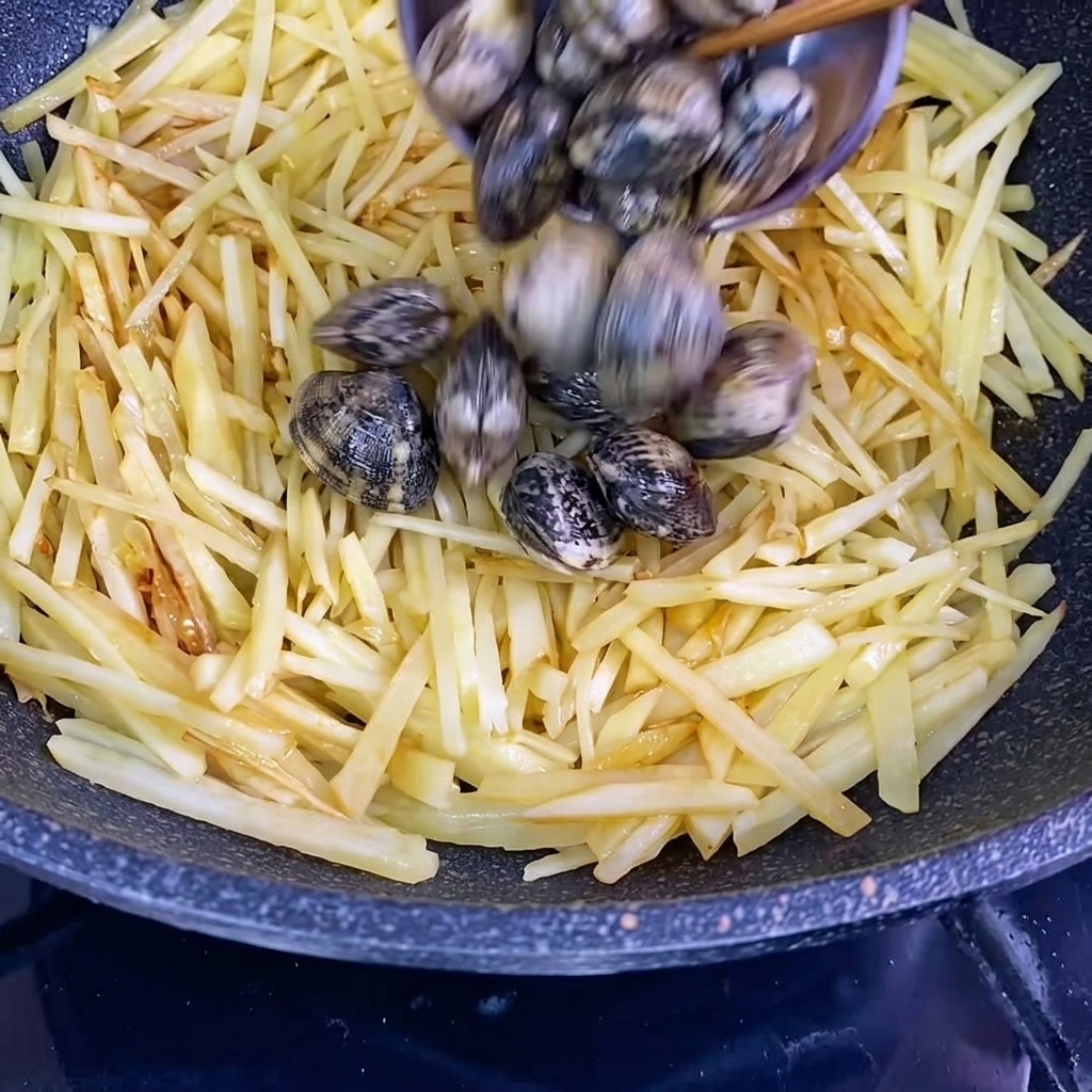 Almejas frescas en su concha añadiéndose al wok con las tiras de papa sazonadas.