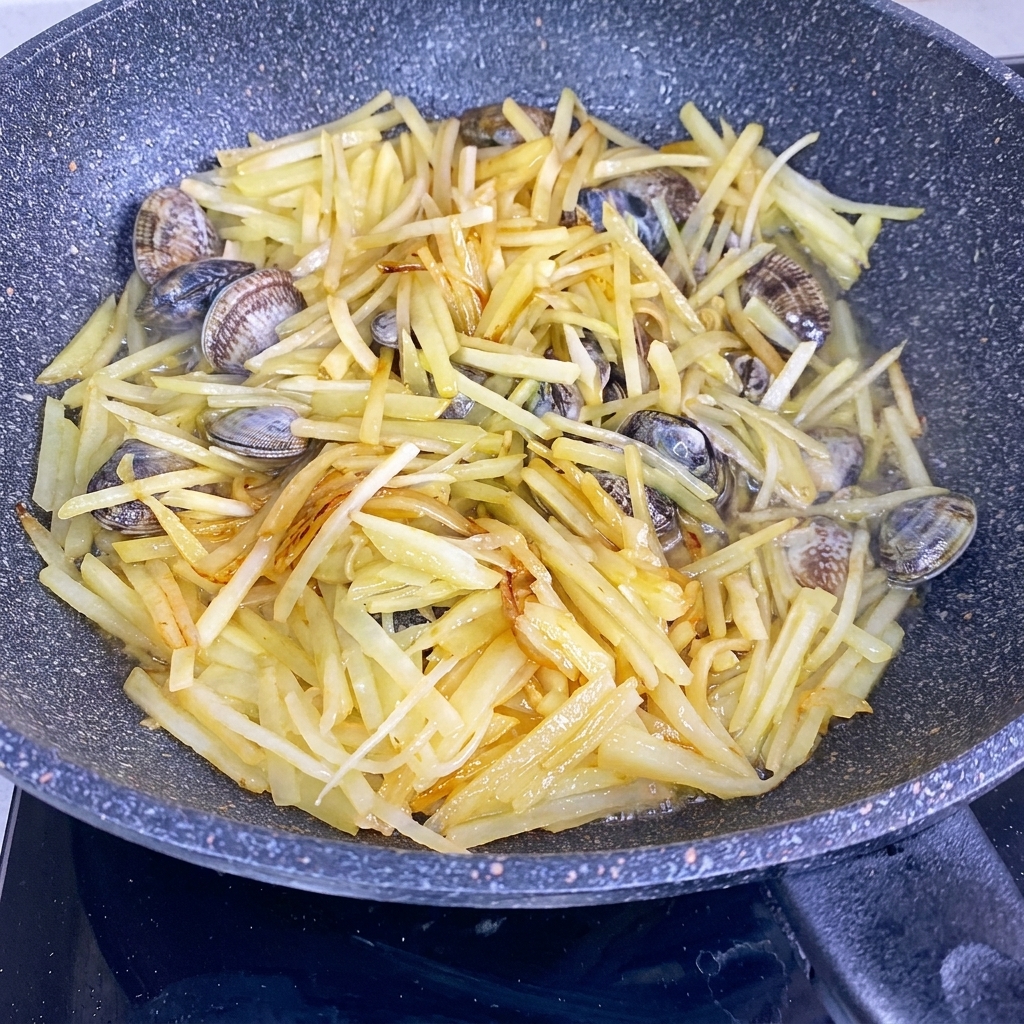 Agua vertiéndose en un wok que contiene tiras de papa salteadas y almejas frescas.