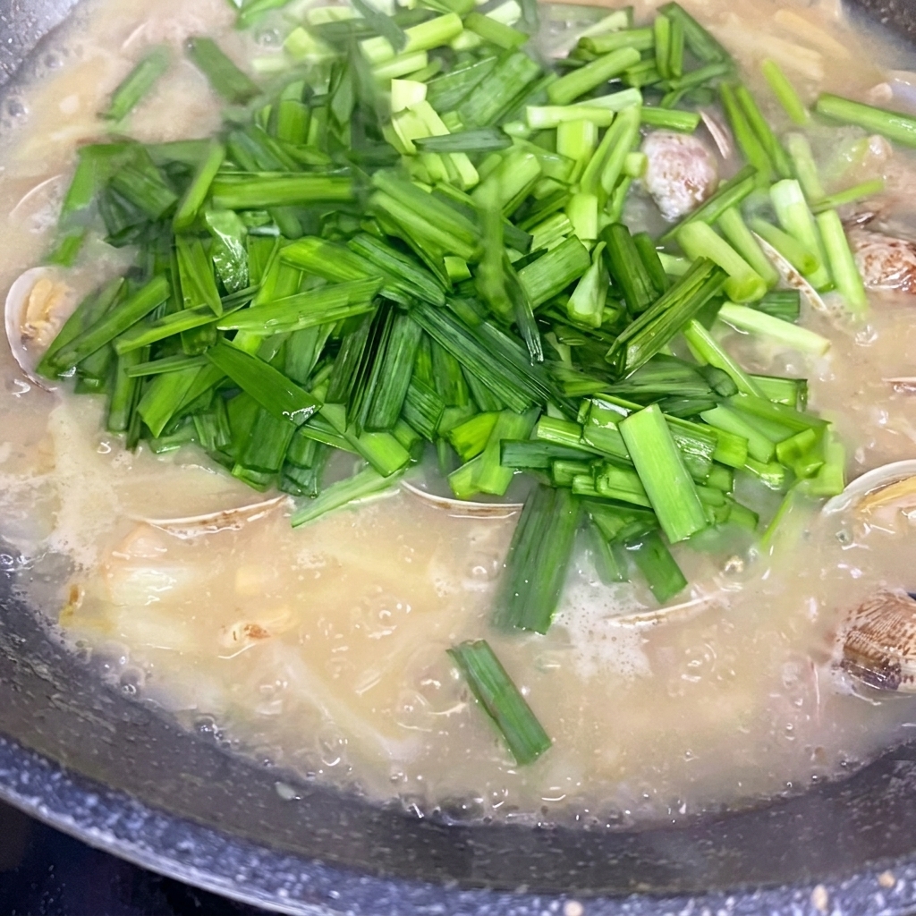 Cebollino chino fresco picado espolvoreándose sobre una olla de sopa de papas y almejas a fuego lento.