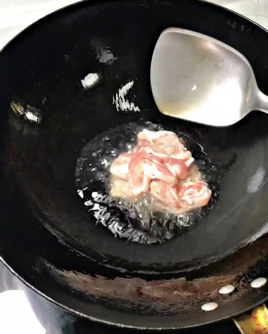 Lonchas finas de cerdo salteándose en un wok caliente con aceite, removidas con una espátula de metal.