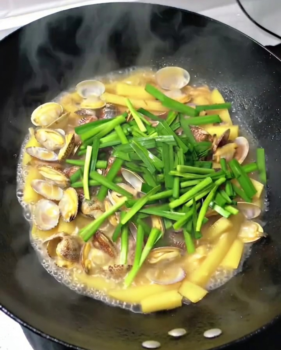 Cebollino al ajo fresco picado siendo esparcido en el wok sobre las almejas, las patatas y el cerdo.