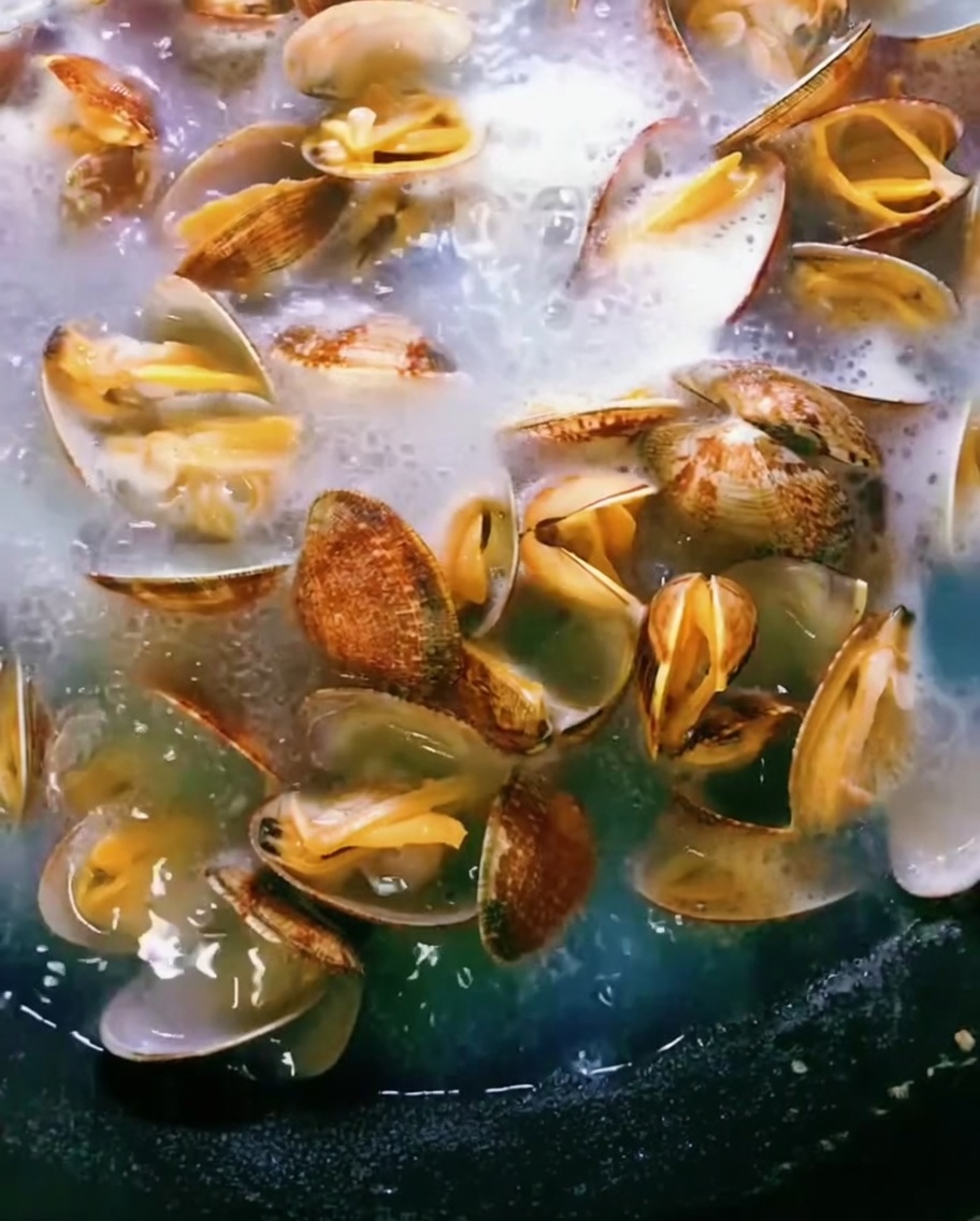 Almejas en una olla con agua hirviendo, con las conchas abriéndose mientras se cocinan.