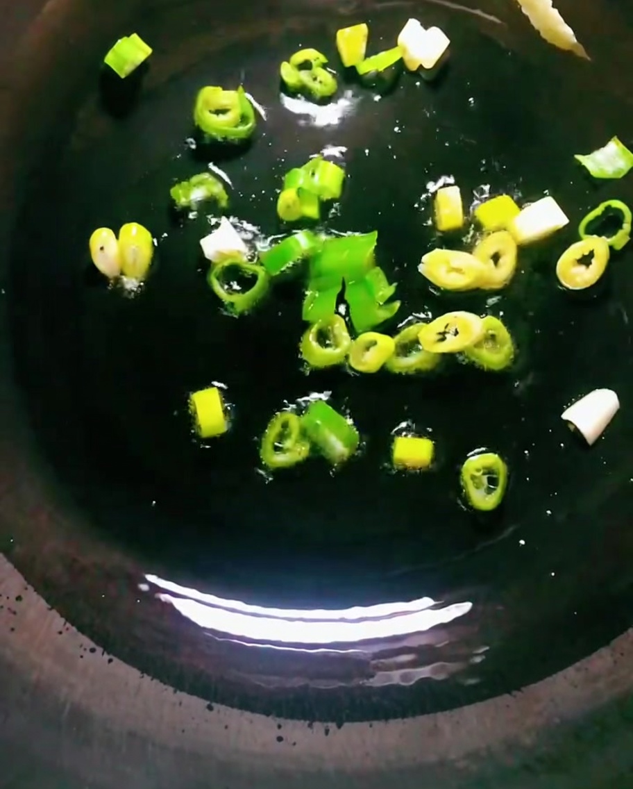 Cebolletas friéndose en aceite caliente en un wok oscuro.